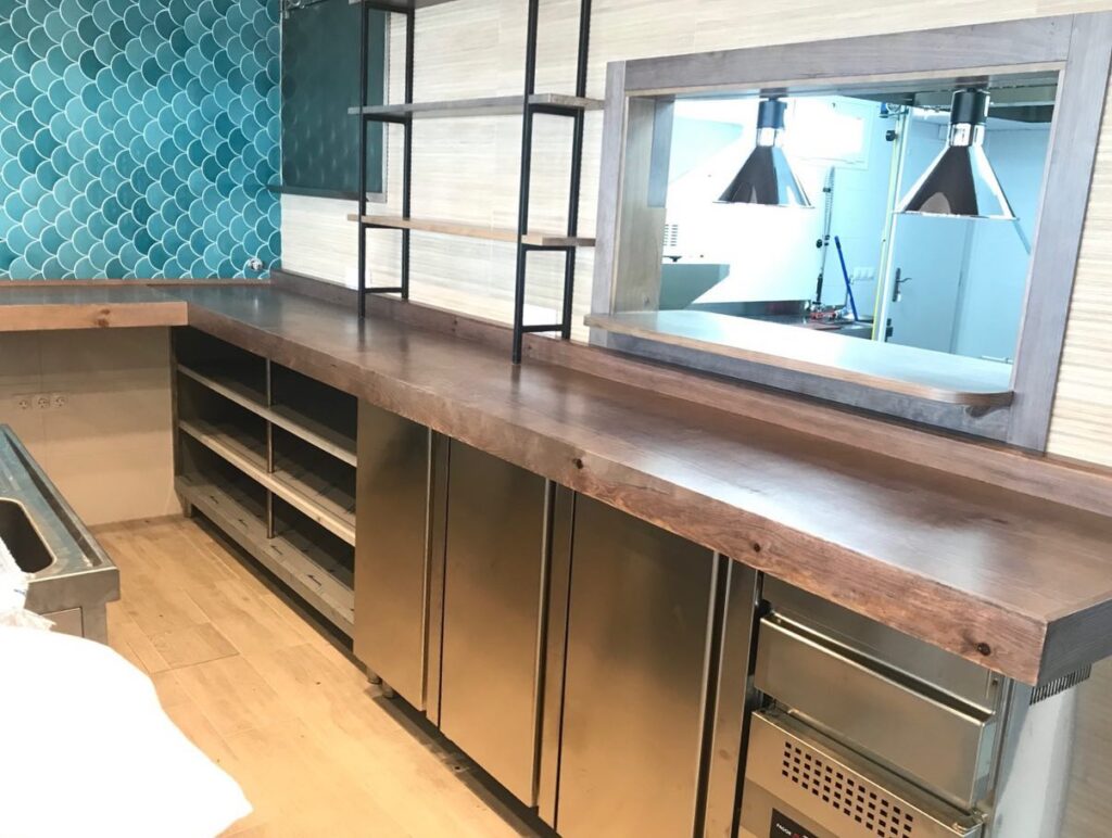 Frentemostrador refrigerado y mueble estantería con encimera de madera natural..